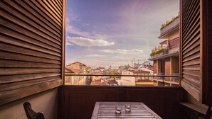 A balcony with a wooden table and chairs, overlooking a cityscape with buildings and a clear sky.