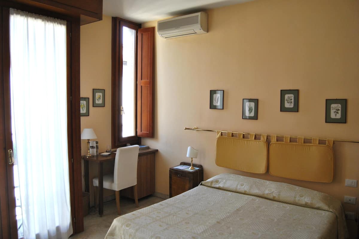 A hotel room with a bed, a desk, a chair, a nightstand, and a window with curtains.