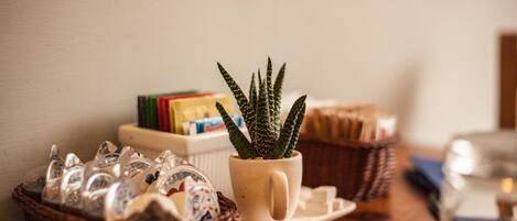 A small potted plant on a table with a basket of glassware and a stack of books.