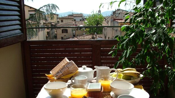 A breakfast setup on a balcony with a view of buildings and a tree.