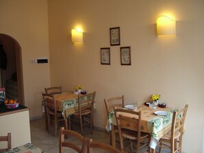 A dining area with wooden chairs and tables, two wall-mounted lights, and framed botanical prints on the wall. - B&B A Teatro (Florence)