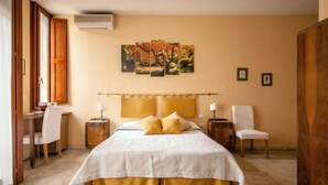 A hotel room with a large bed, a desk, a chair, and a painting on the wall.