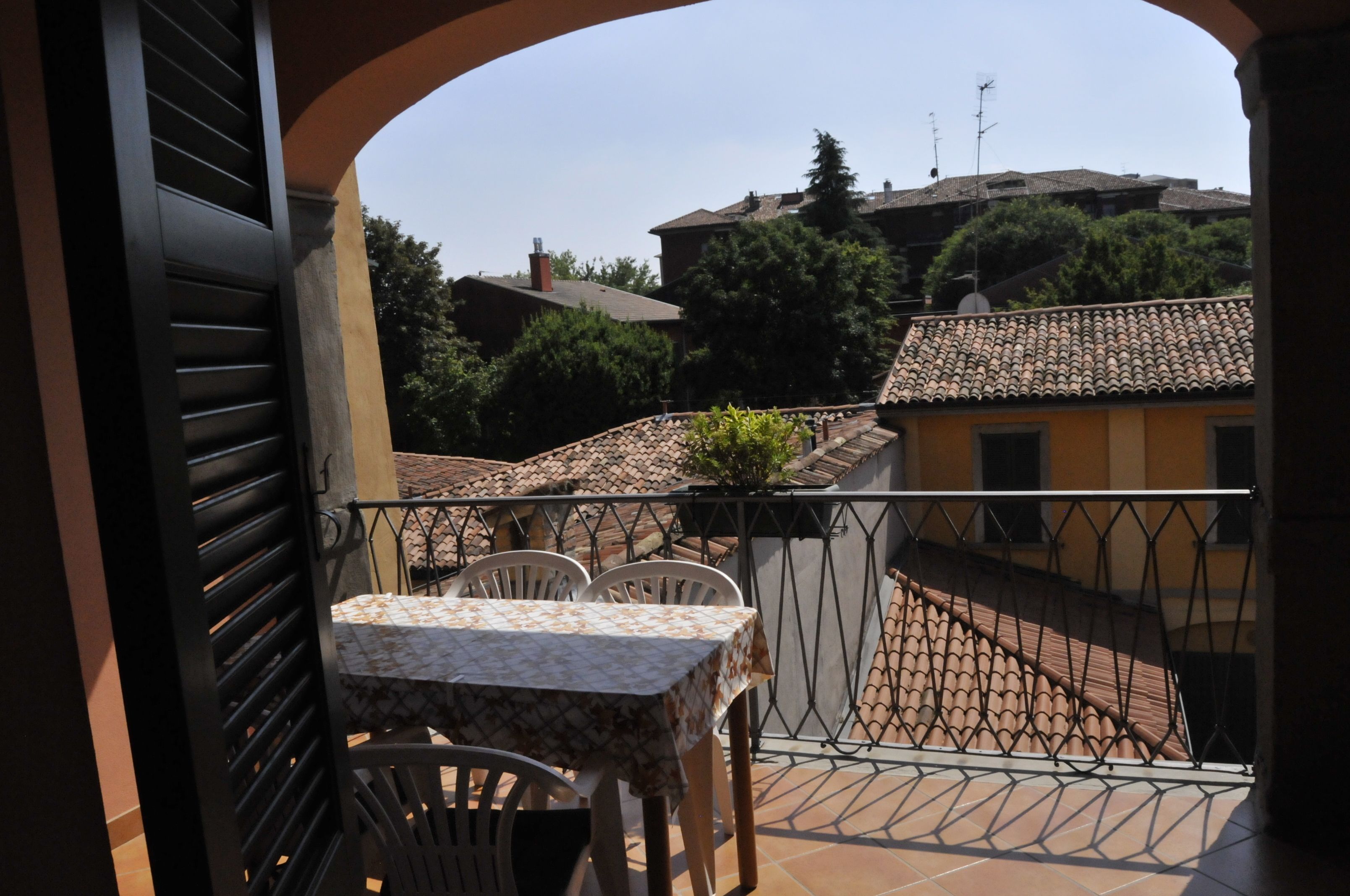 Un balcone con tavolo e sedie, un tetto in tegole e edifici sullo sfondo.