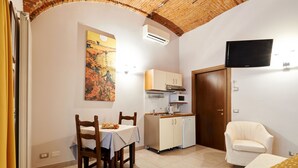 Cozinha compacta com mesa, cadeiras, micro-ondas e televisão presa na parede.
