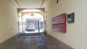 Corredor com piso de pedra que leva a uma entrada com portão, caixa de correio e câmera de segurança na parede.