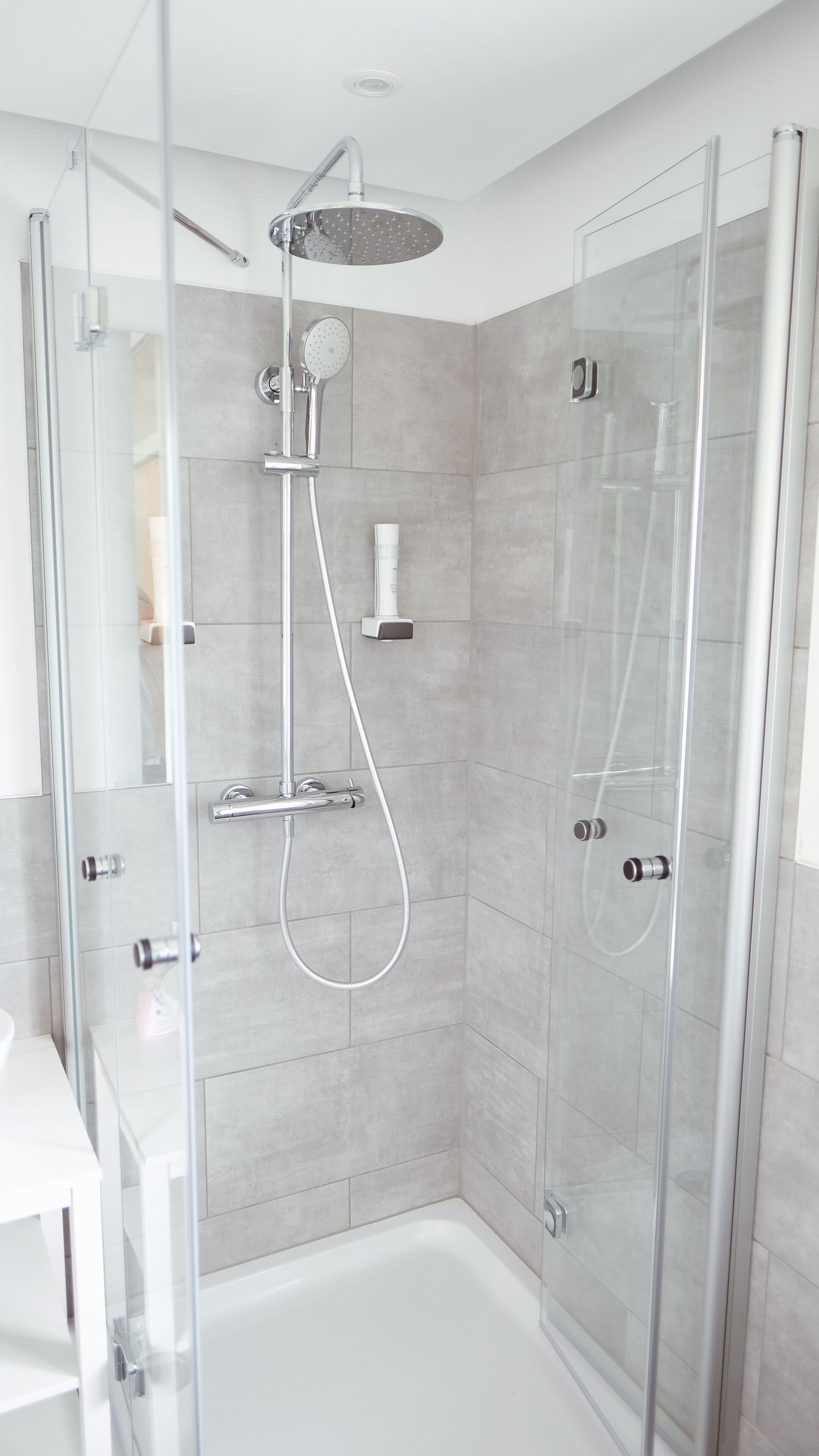 Une cabine de douche moderne dotée d’une porte en verre, d’un pommeau de douche à main et d’un robinet mural.
