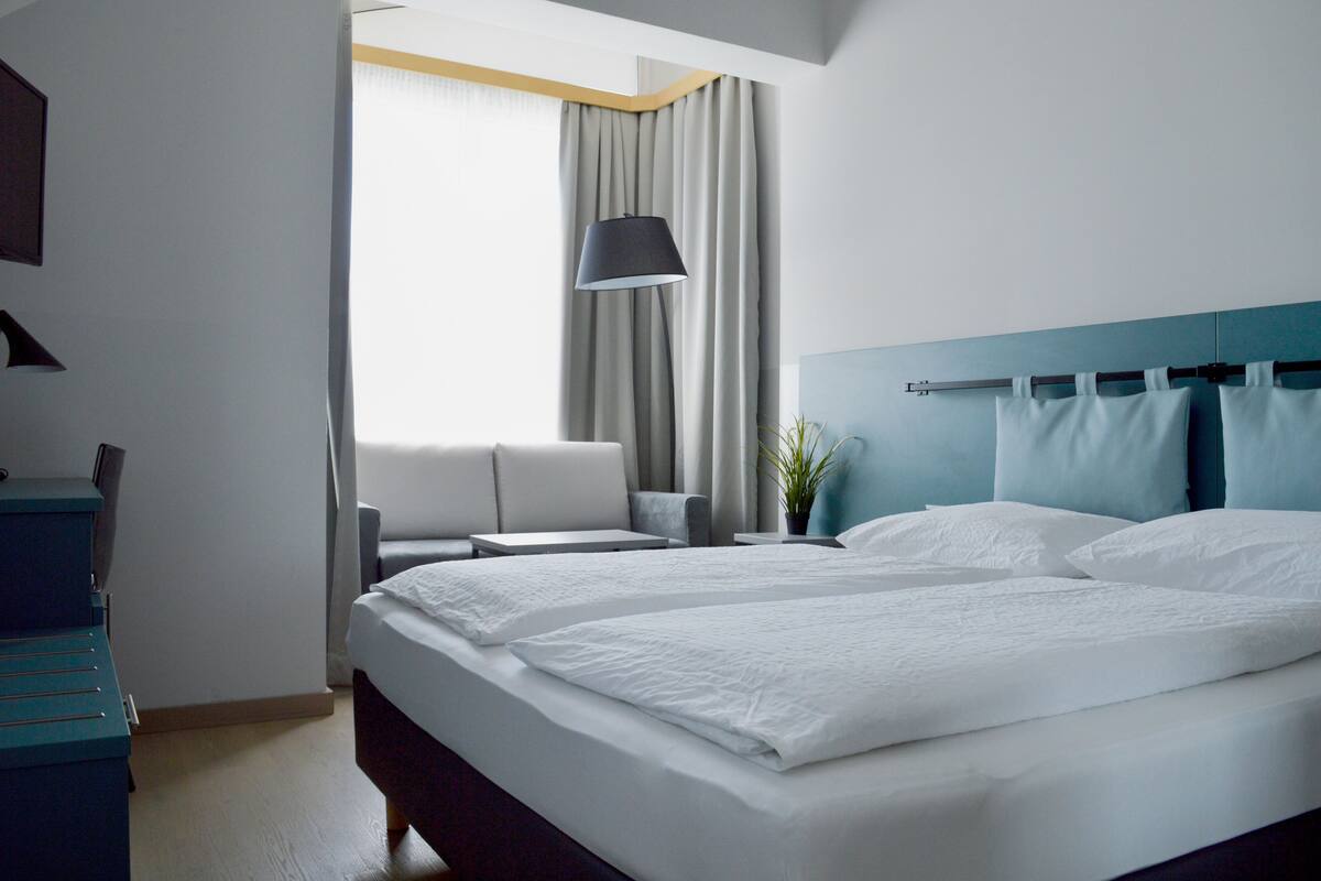 Moderni hotellihuone, jossa on suuri sänky, sohva, työpöytä ja lamppu.