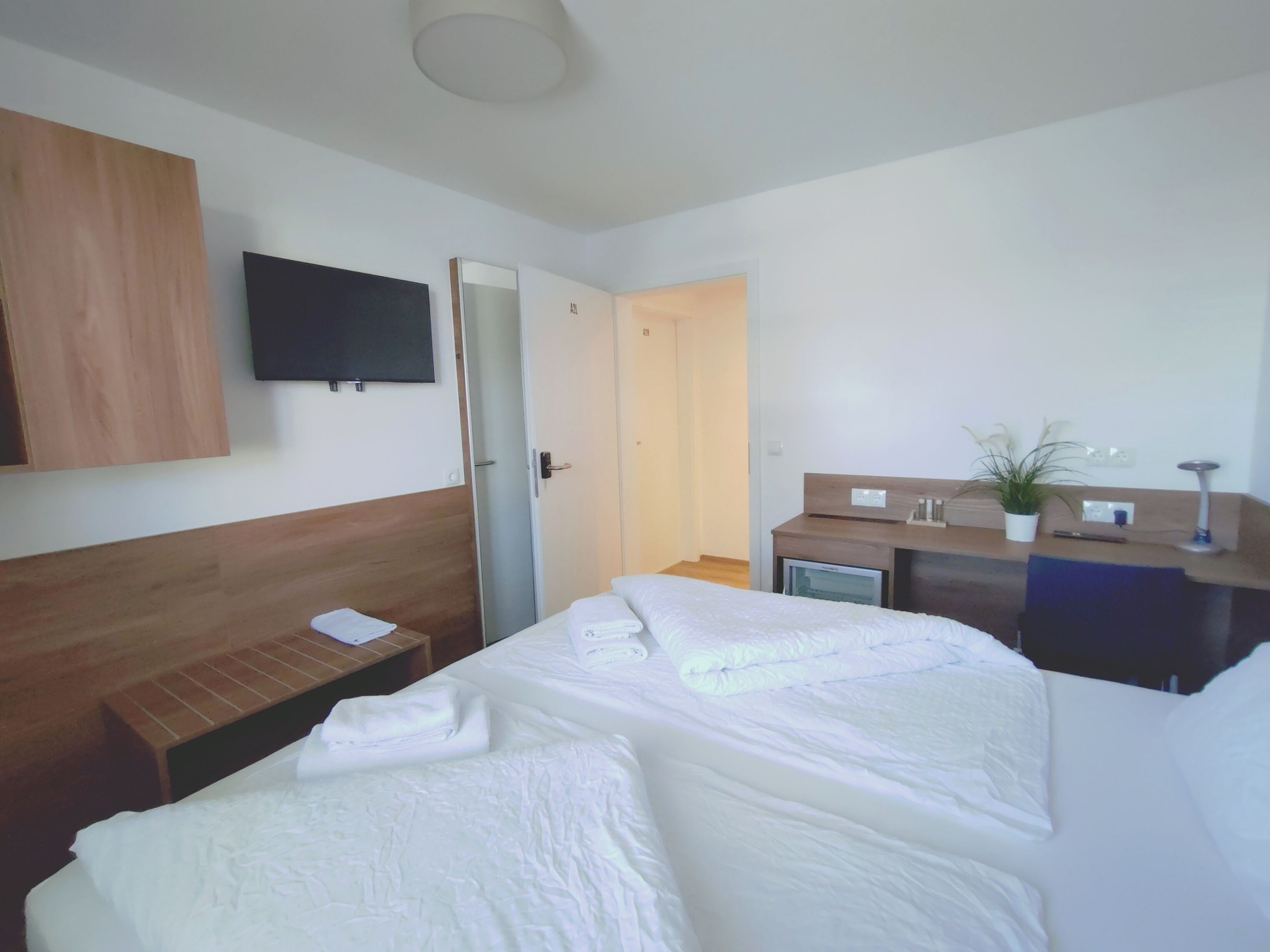 A hotel room with a bed, a desk, a television, and a door.