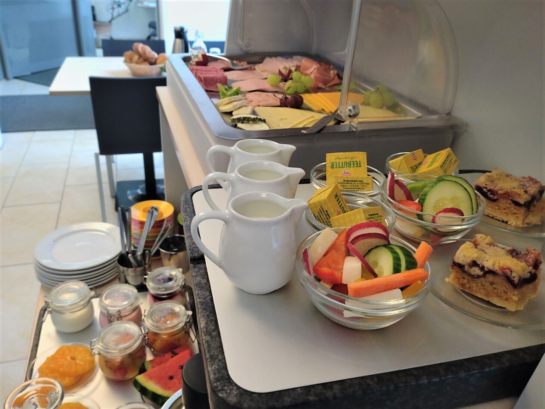 Una barra de buffet con diversos alimentos, entre ellos frutas, verduras, quesos y sándwiches.