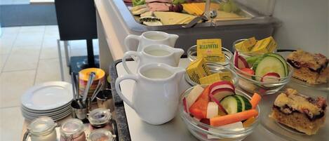 Una barra de buffet con diversos alimentos, entre ellos frutas, verduras, quesos y sándwiches.