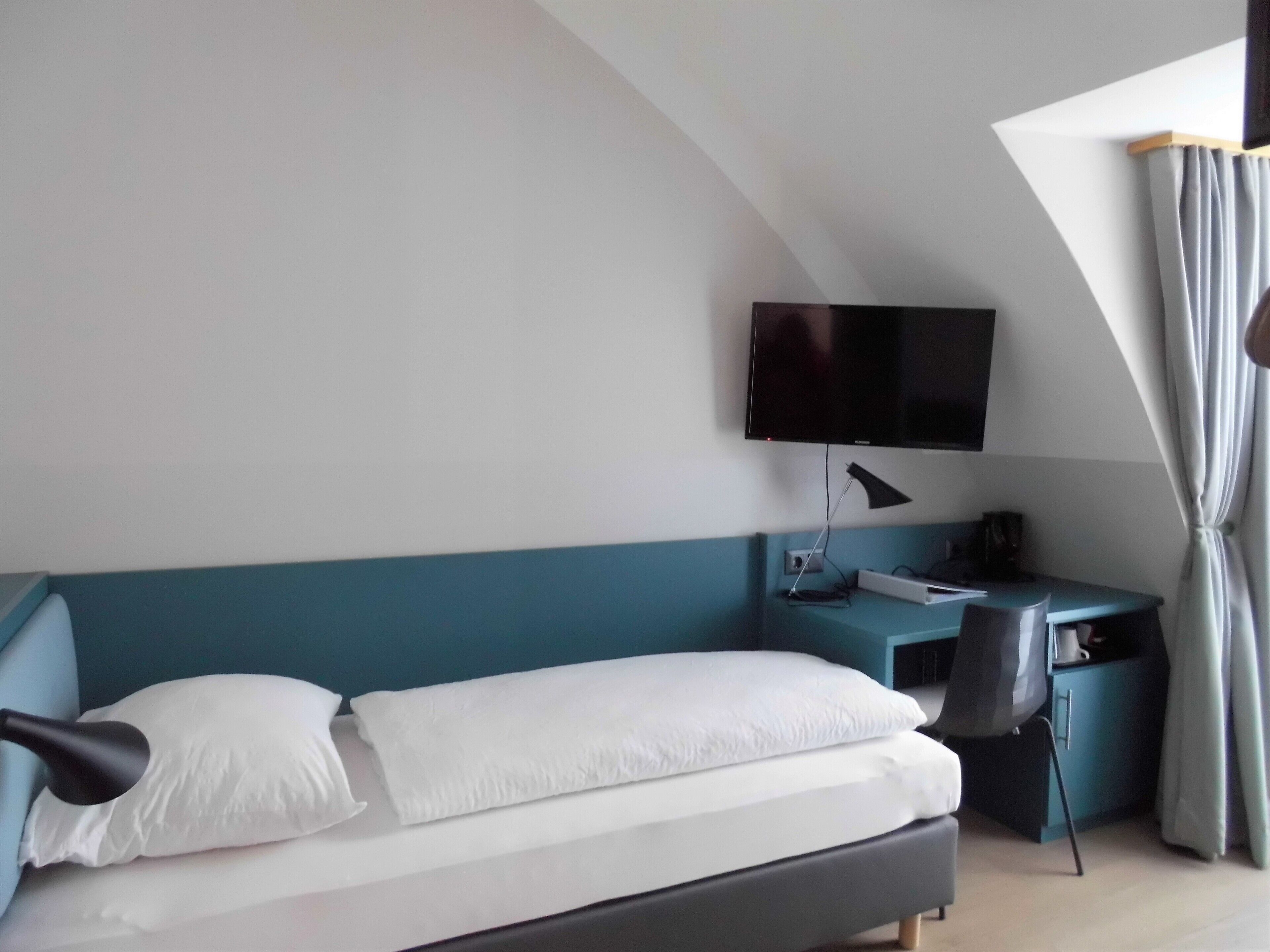 A hotel room with a bed, a desk, a chair, a TV, and a window with curtains.