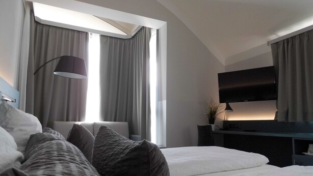 Un dormitorio moderno con una cama grande, un escritorio con computadora y un televisor montado en la pared.