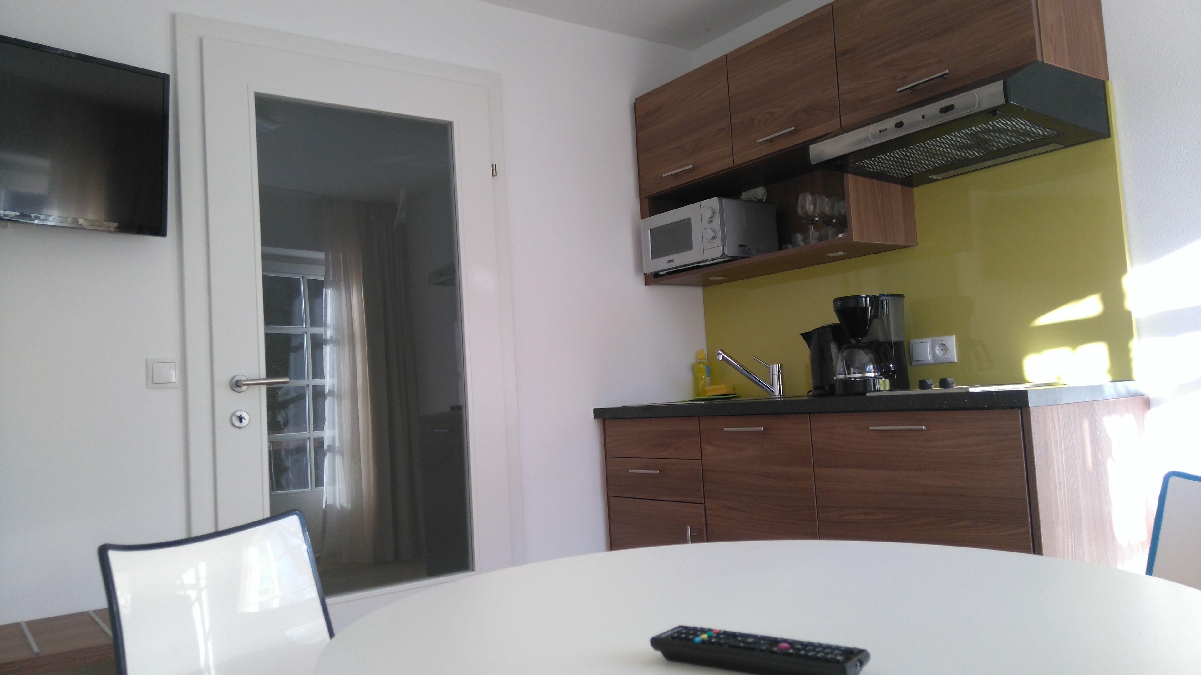 A compact kitchen with wooden cabinets, a microwave, a coffee maker, and a dining area with a table and chairs.