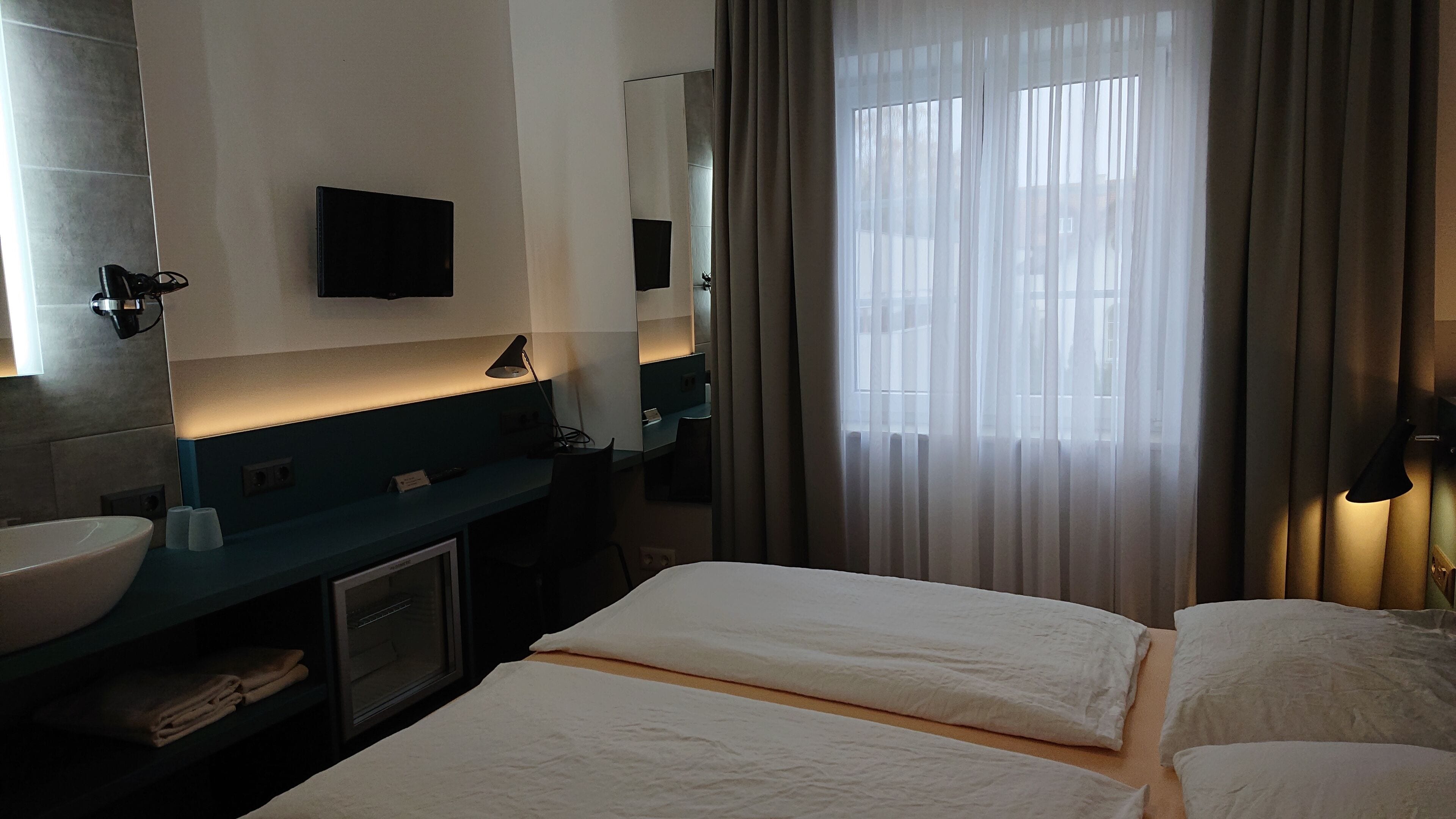 A hotel room with a bed, a sink, a mirror, and a window with curtains.