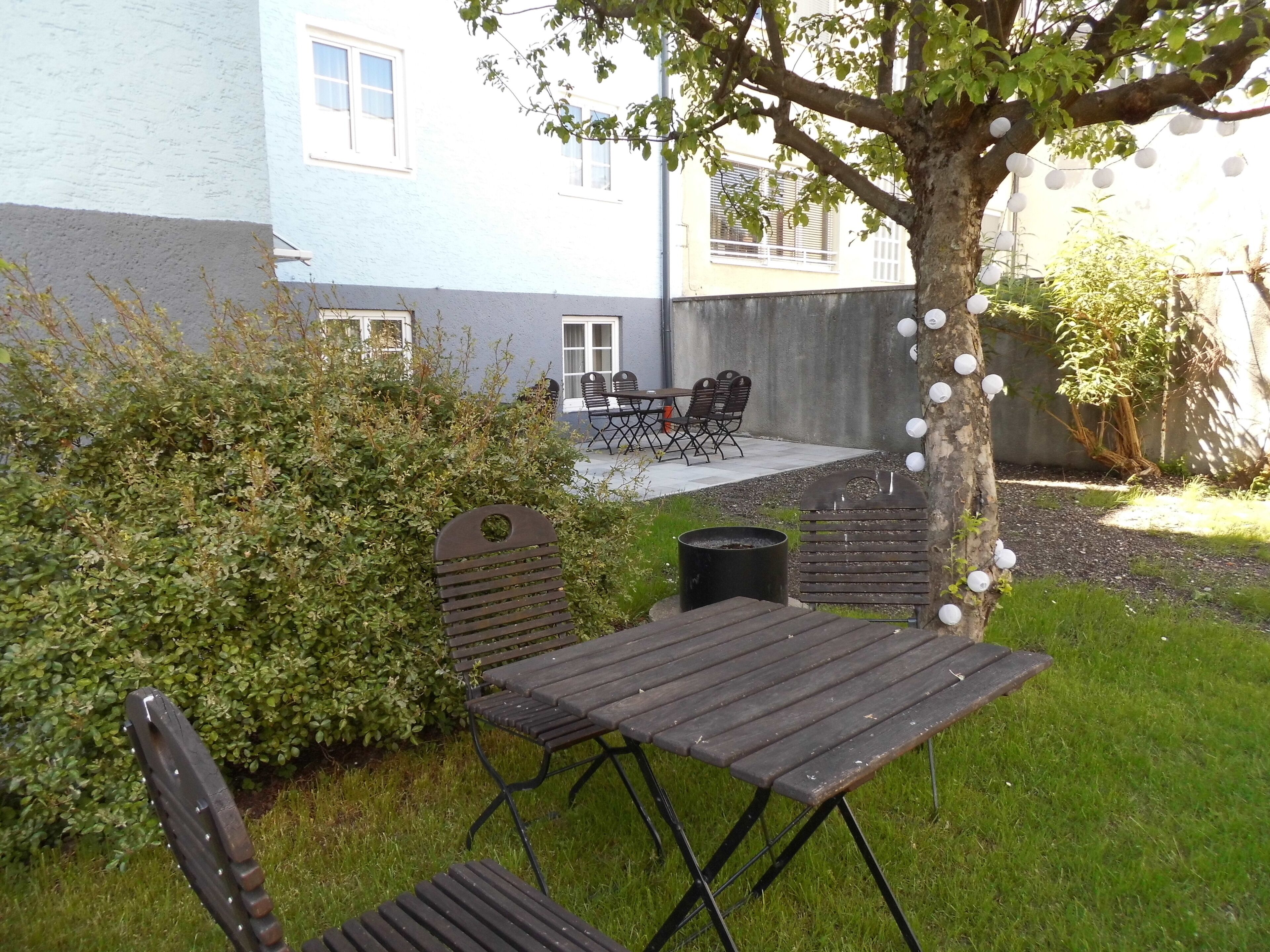 A patio area with a table and chairs, a small tree, and a hedge.