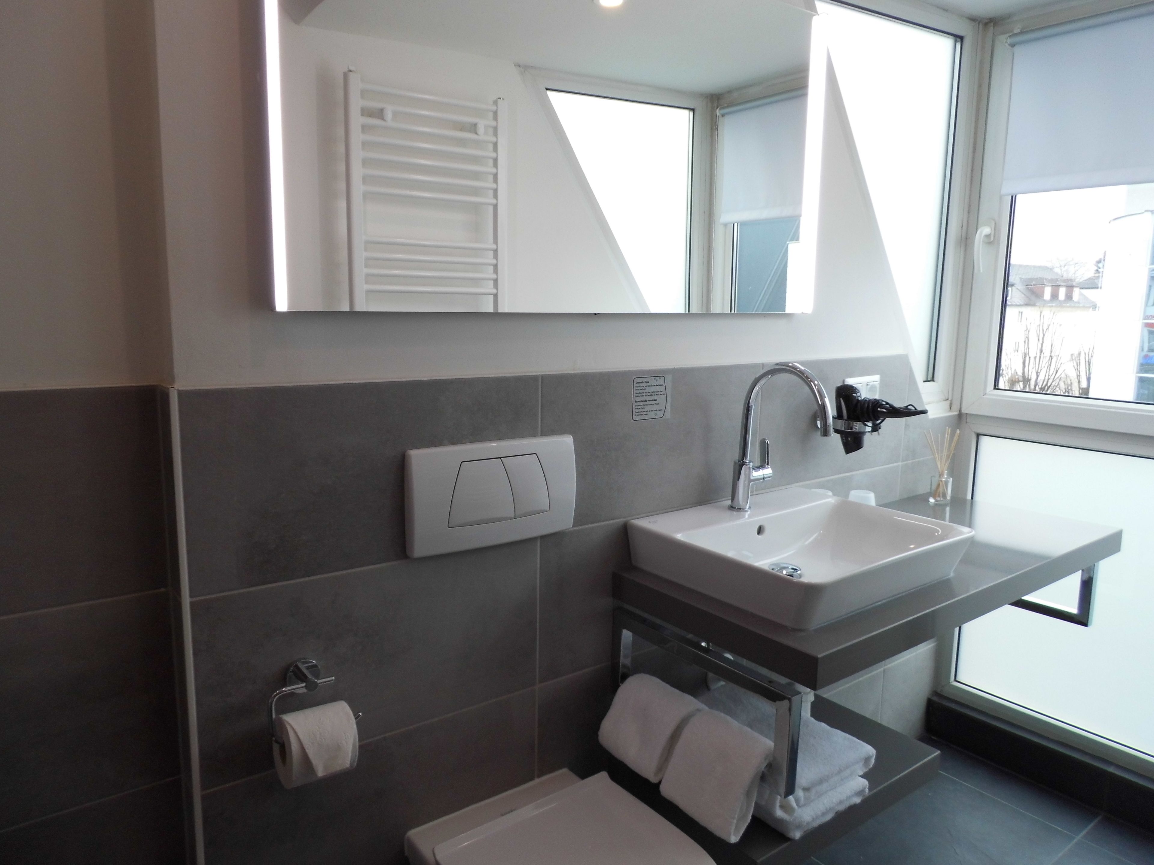 A modern bathroom with a large mirror, a white sink, and a towel rack.