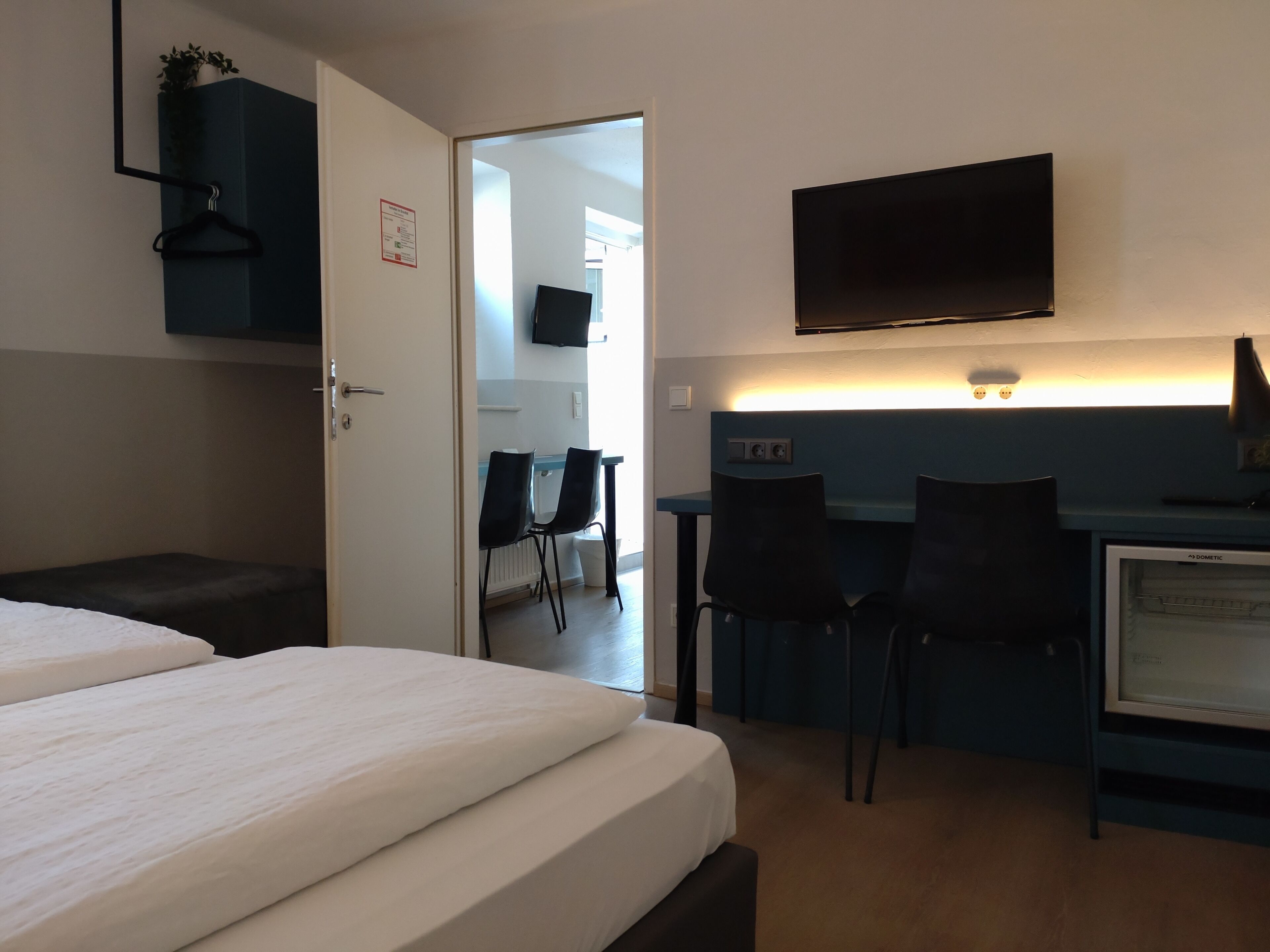 Ett hotellrum med en säng, ett skrivbord, två stolar, en tv och ett litet kylskåp.