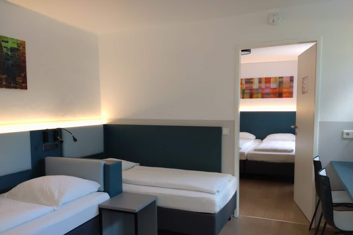 Hotellihuone, jossa on kaksi erillistä sänkyä, pieni pöytä, työpöytä ja tuoli.