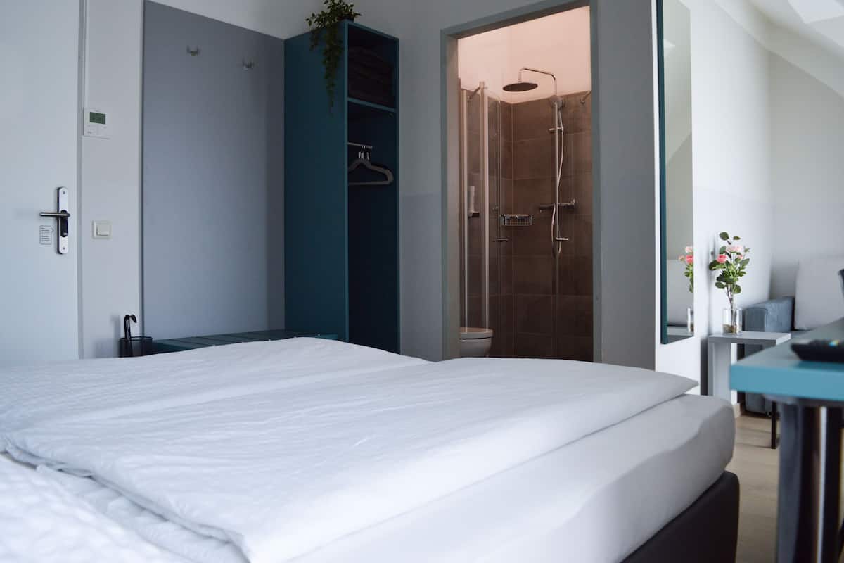 Moderni hotellihuone, jossa on suuri sänky, suihkutila, työpöytä tuolilla sekä pieni oleskelualue, jossa on kasvi.