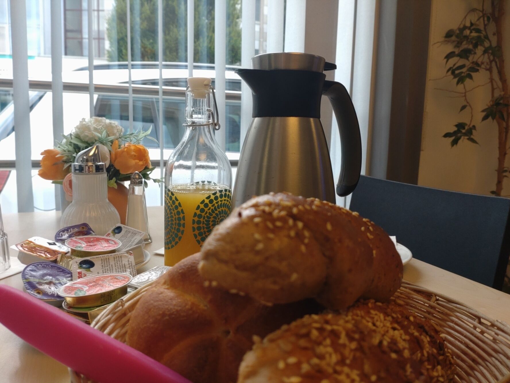 Aamiaispöydällä on croissant, pullo appelsiinimehua, kahvipannu ja erilaisia mausteita.