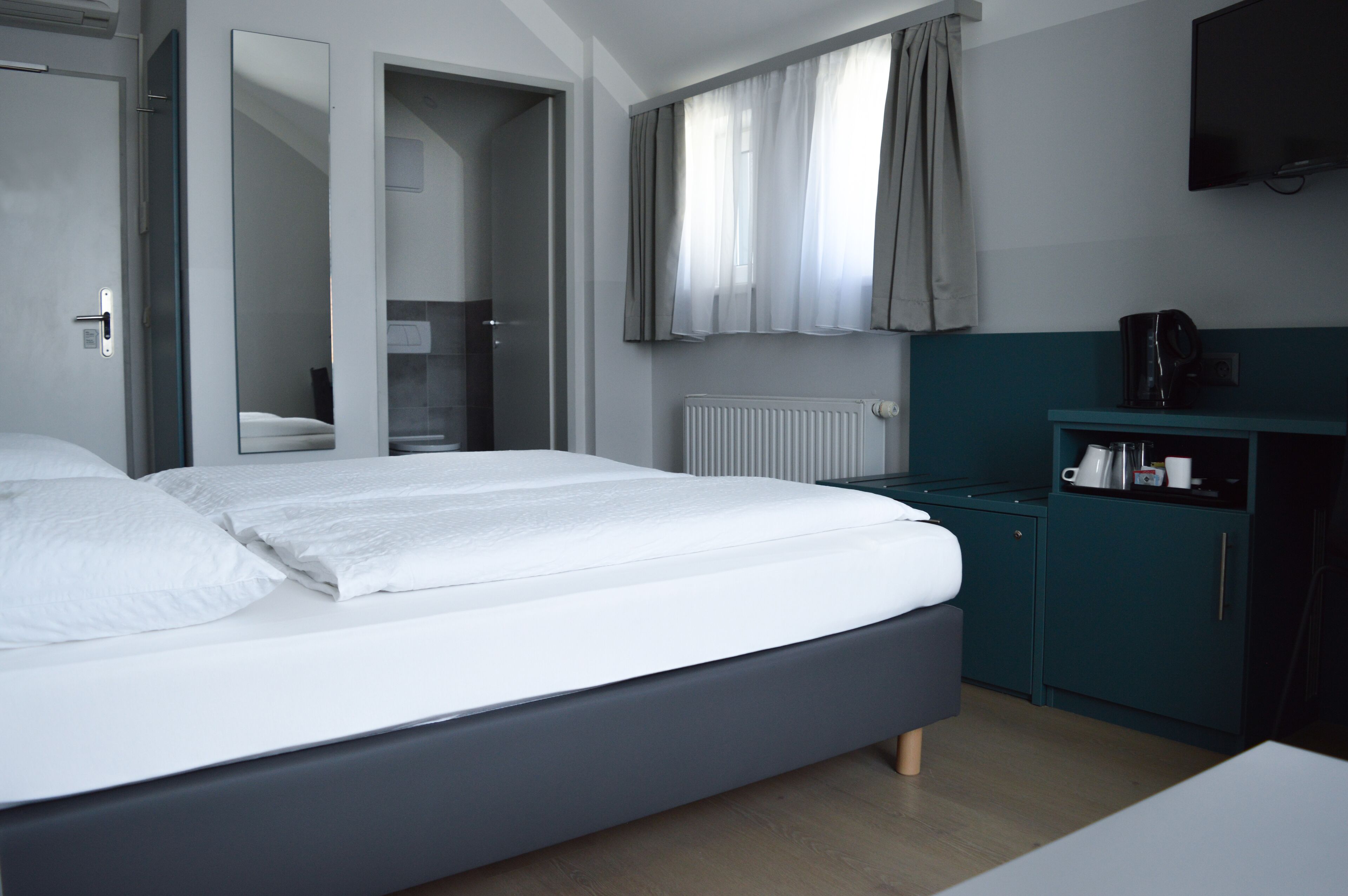 Une chambre d’hôtel moderne avec un grand lit, une salle de bain visible à travers une porte ouverte, un téléviseur fixé au mur et un petit coin cuisine.