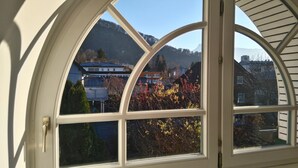 Vista a través de una ventana con marco blanco, mostrando un edificio con techo azul y una montaña al fondo.