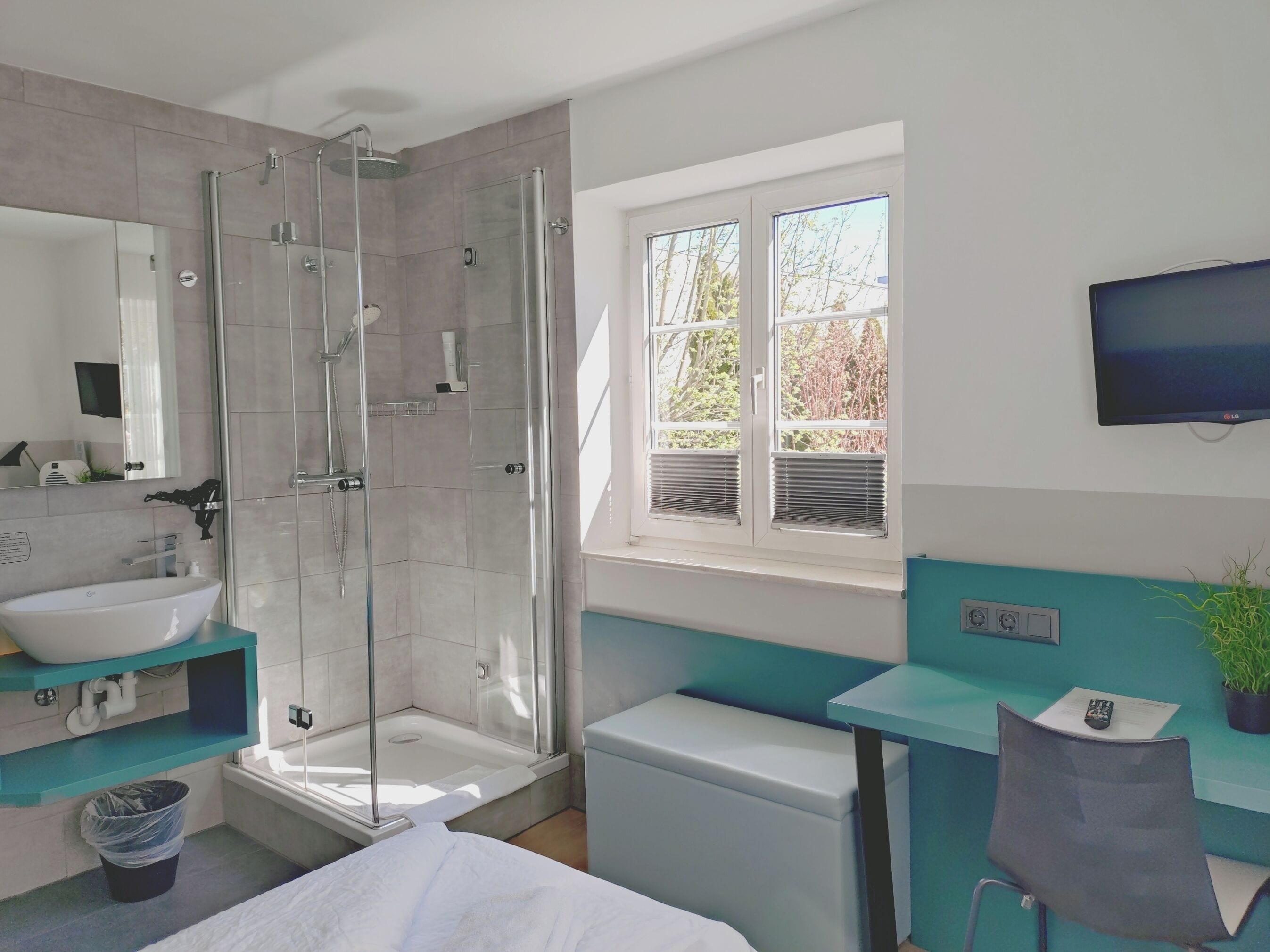 Une salle de bain moderne dotée d’une douche à parois de verre, d’un lavabo, de toilettes et d’une fenêtre laissant entrer la lumière naturelle.