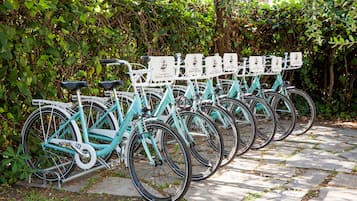 A row of teal bicycles with white racks, each labeled with a name, parked on a stone path.