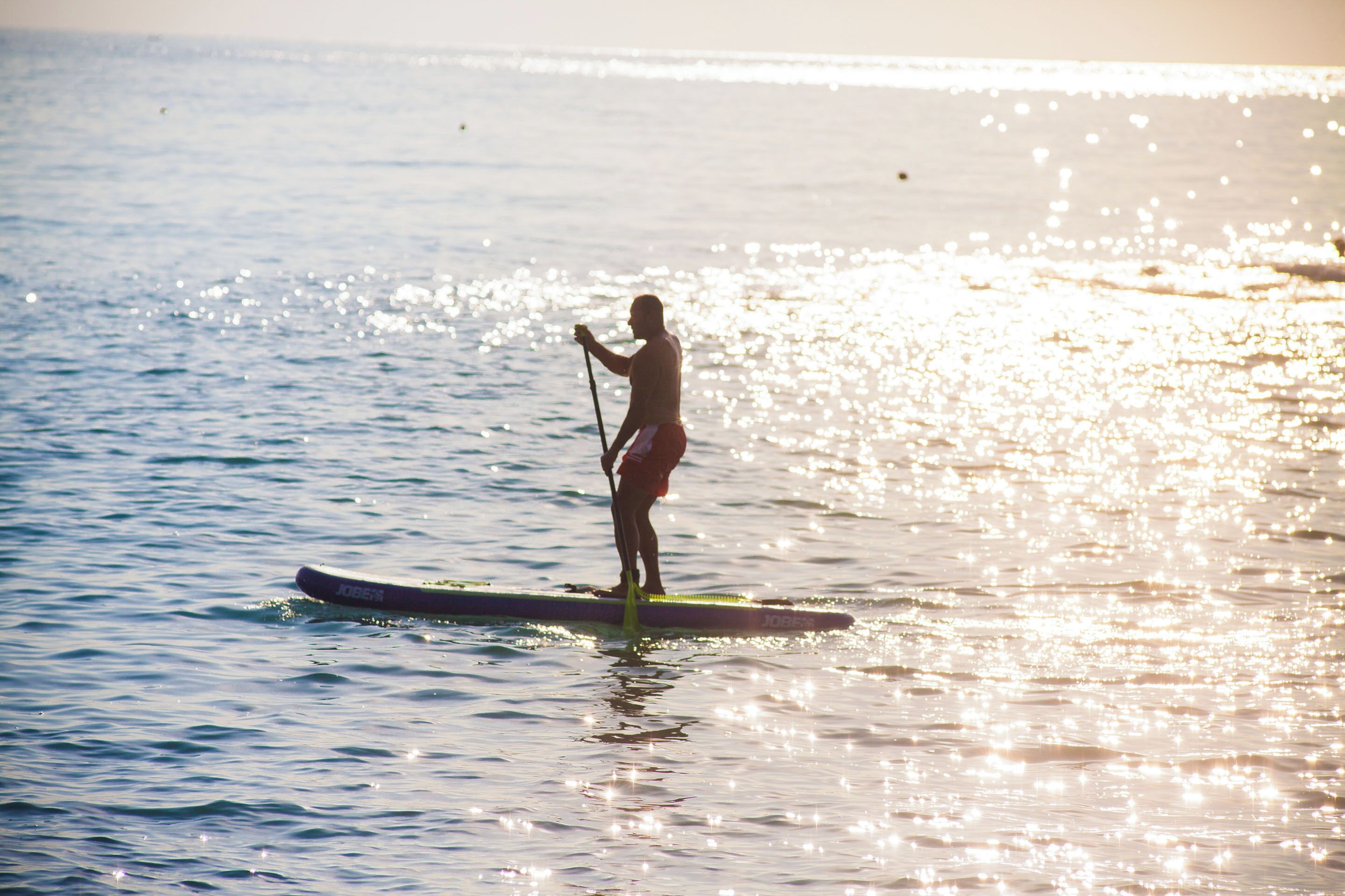 Une personne pratiquant le paddle sur une eau calme, avec un coucher de soleil en arrière-plan.