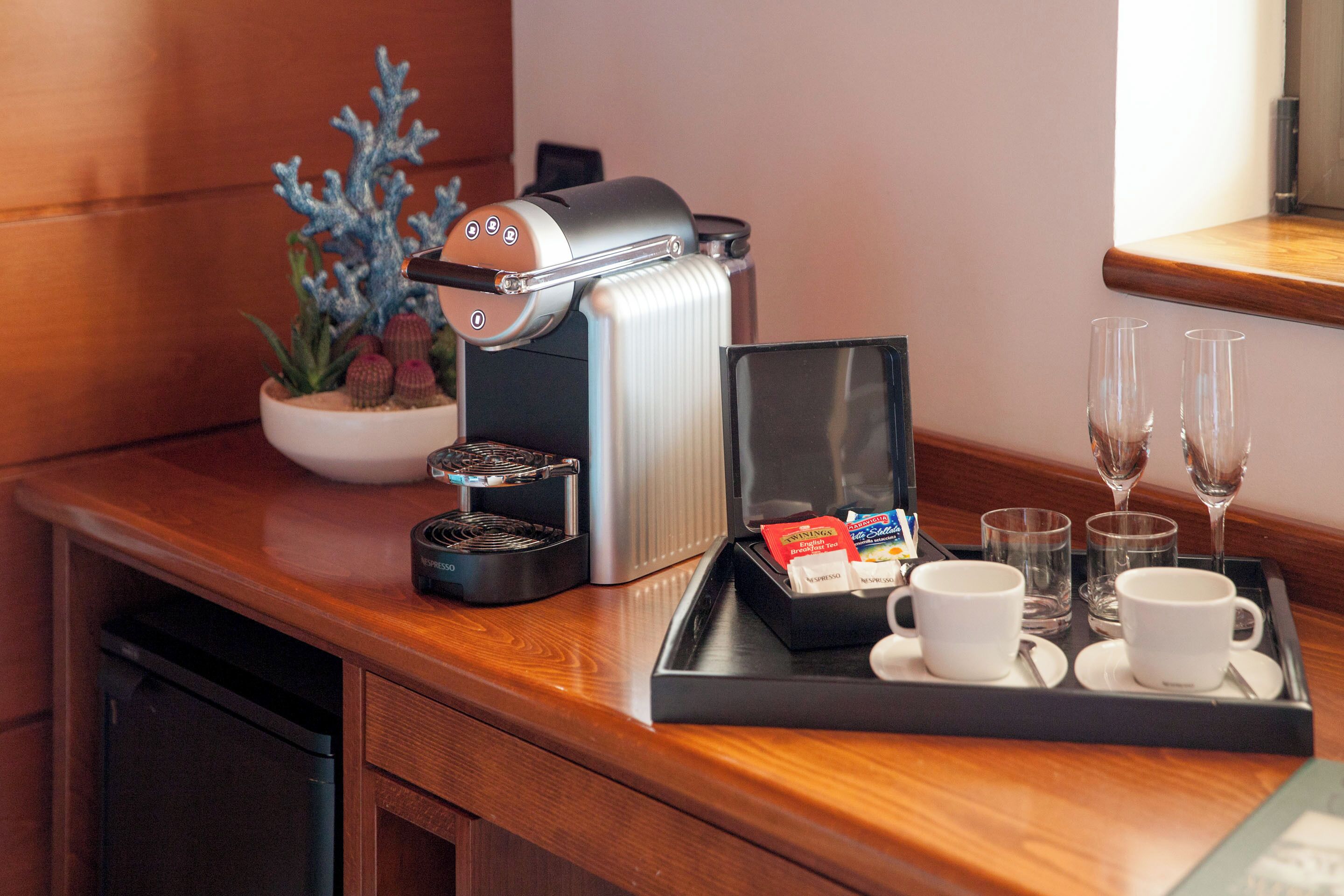 Une machine à café, un plateau avec des tasses et des verres, et une petite plante sur un comptoir en bois.