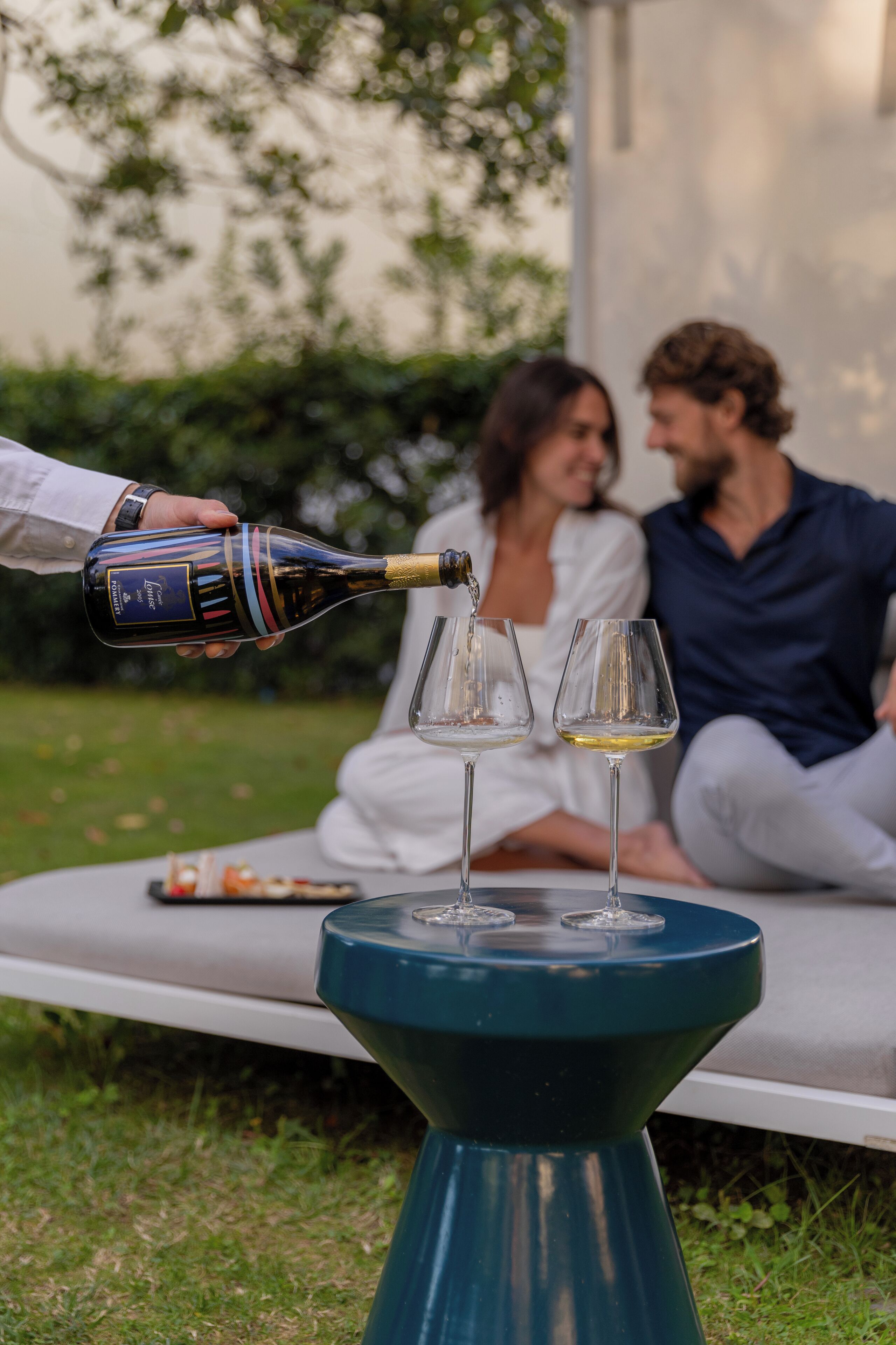 A person pouring wine into two glasses on a table outdoors.