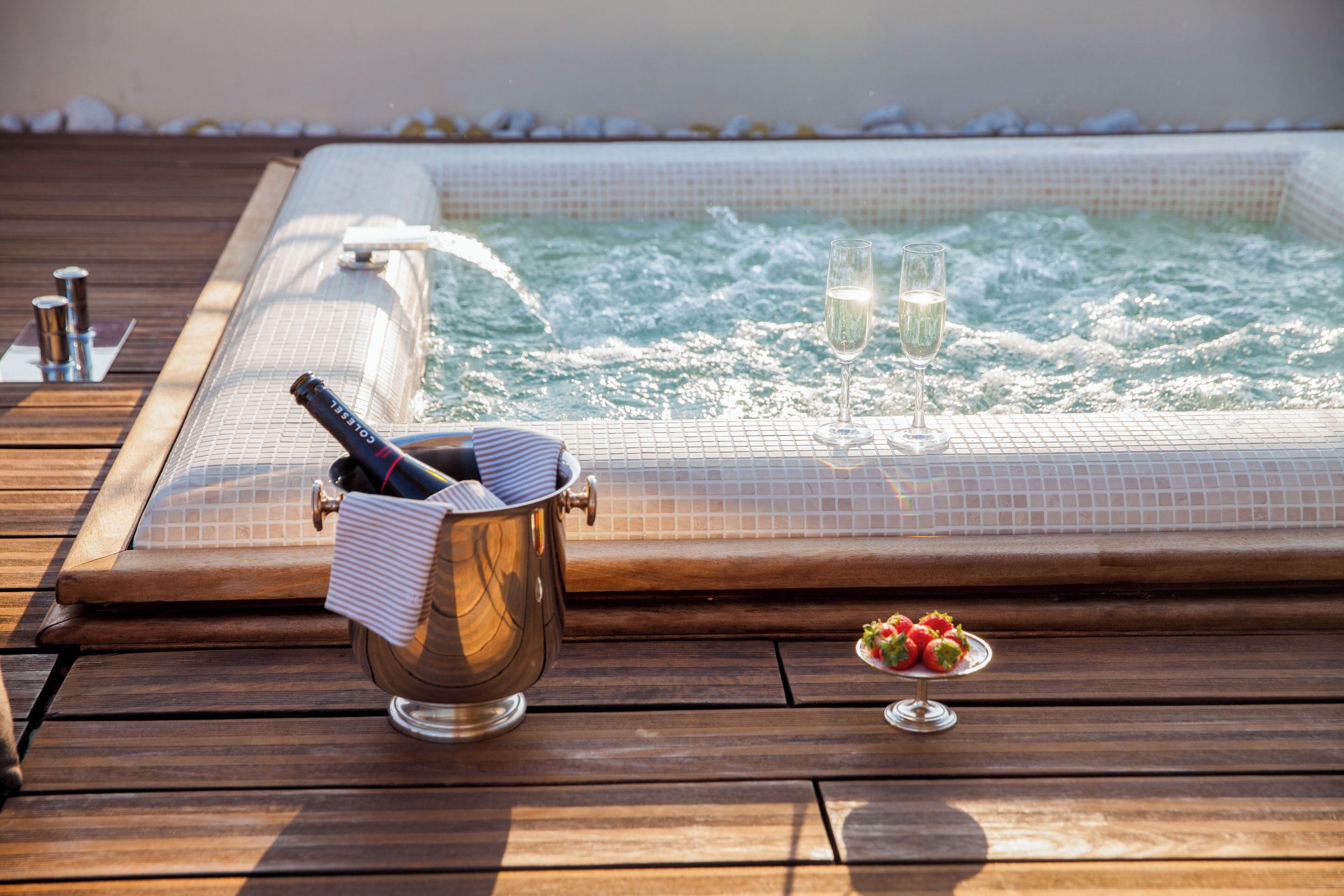 Ein Whirlpool mit Champagner und Erdbeeren auf einer Holzterrasse.