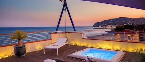 A wooden deck with a hot tub, lounge chairs, and potted plants.