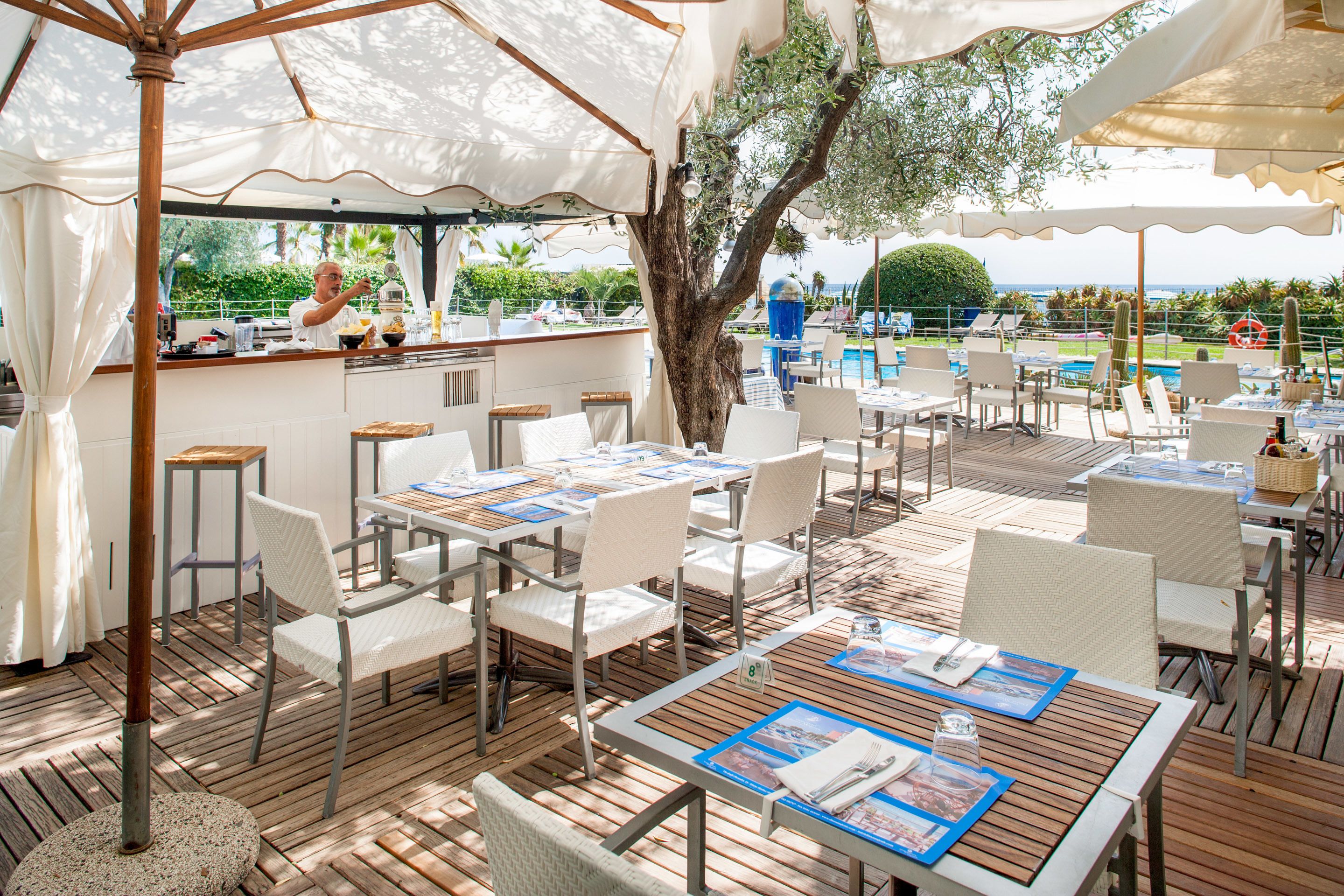 An outdoor dining area with tables and chairs, a bar, and a view of the sea.
