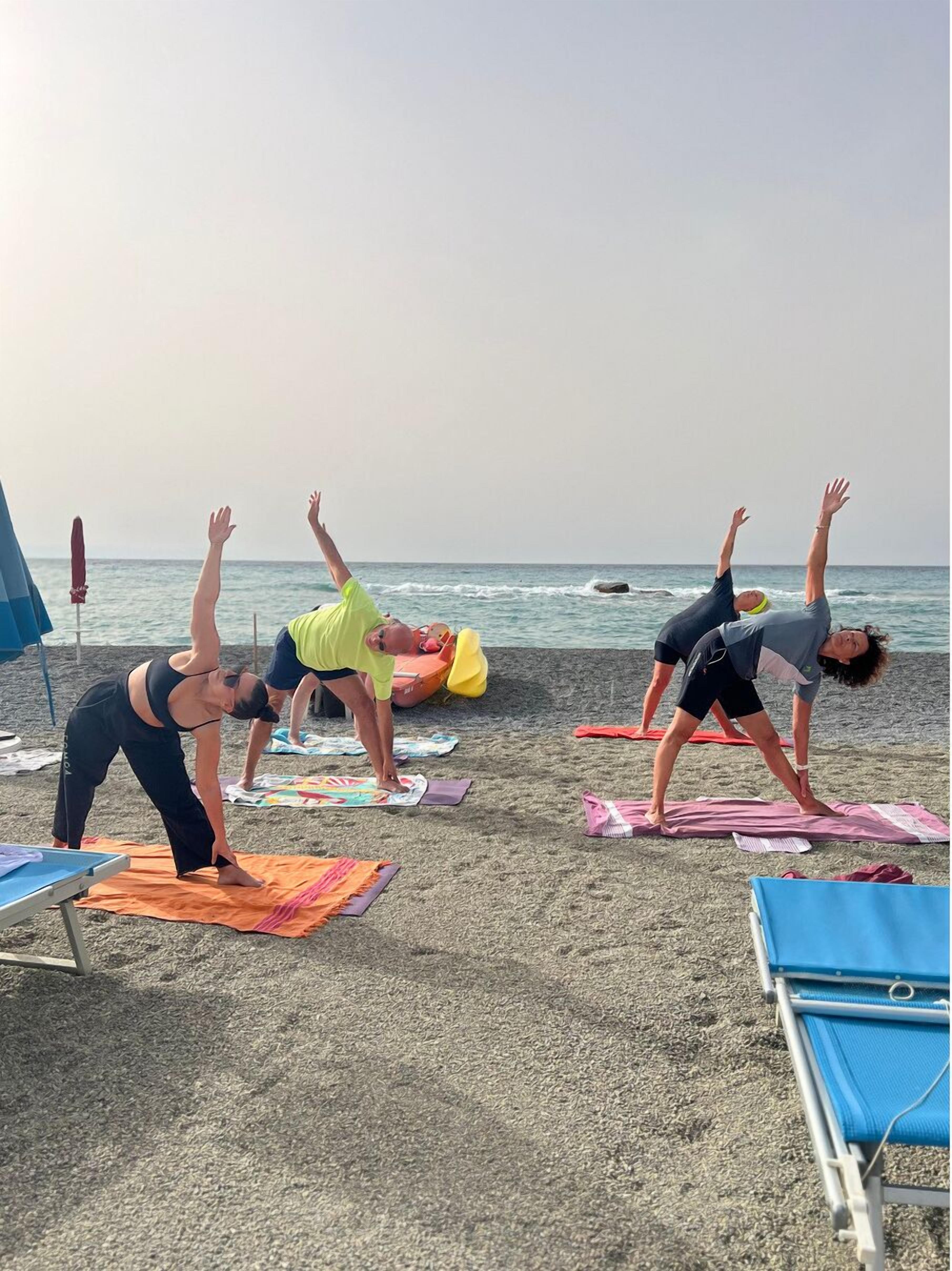 Eine Gruppe von Menschen praktiziert Yoga auf Matten am Strand, mit dem Meer im Hintergrund.