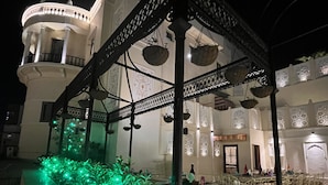 A spacious outdoor area with a covered seating area, a large white building in the background, and decorative lighting. - Hotel Ratnawali (Jaipur)