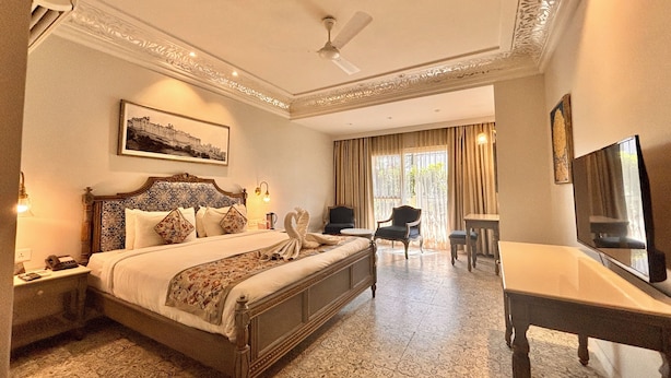 A hotel room with a large bed, a desk, a chair, a television, and a ceiling fan. - Hotel Ratnawali (Jaipur)