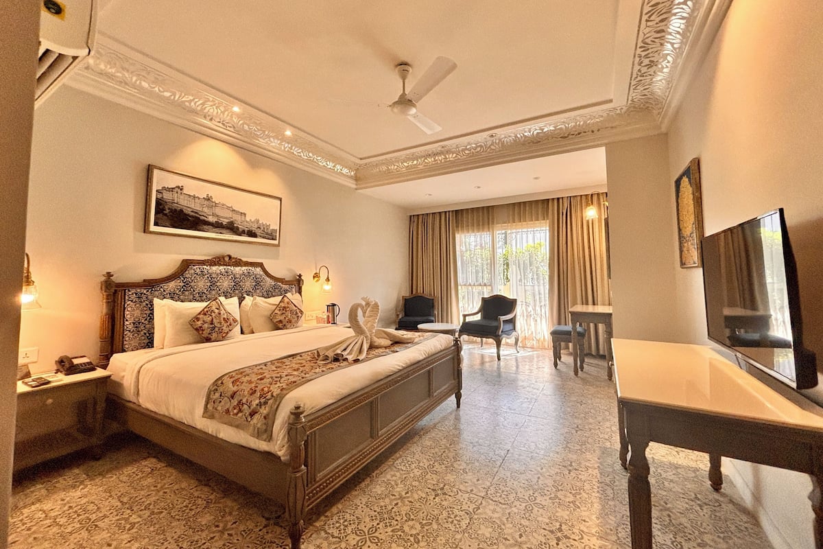 A hotel room with a large bed, a desk, a chair, a television, and a ceiling fan.