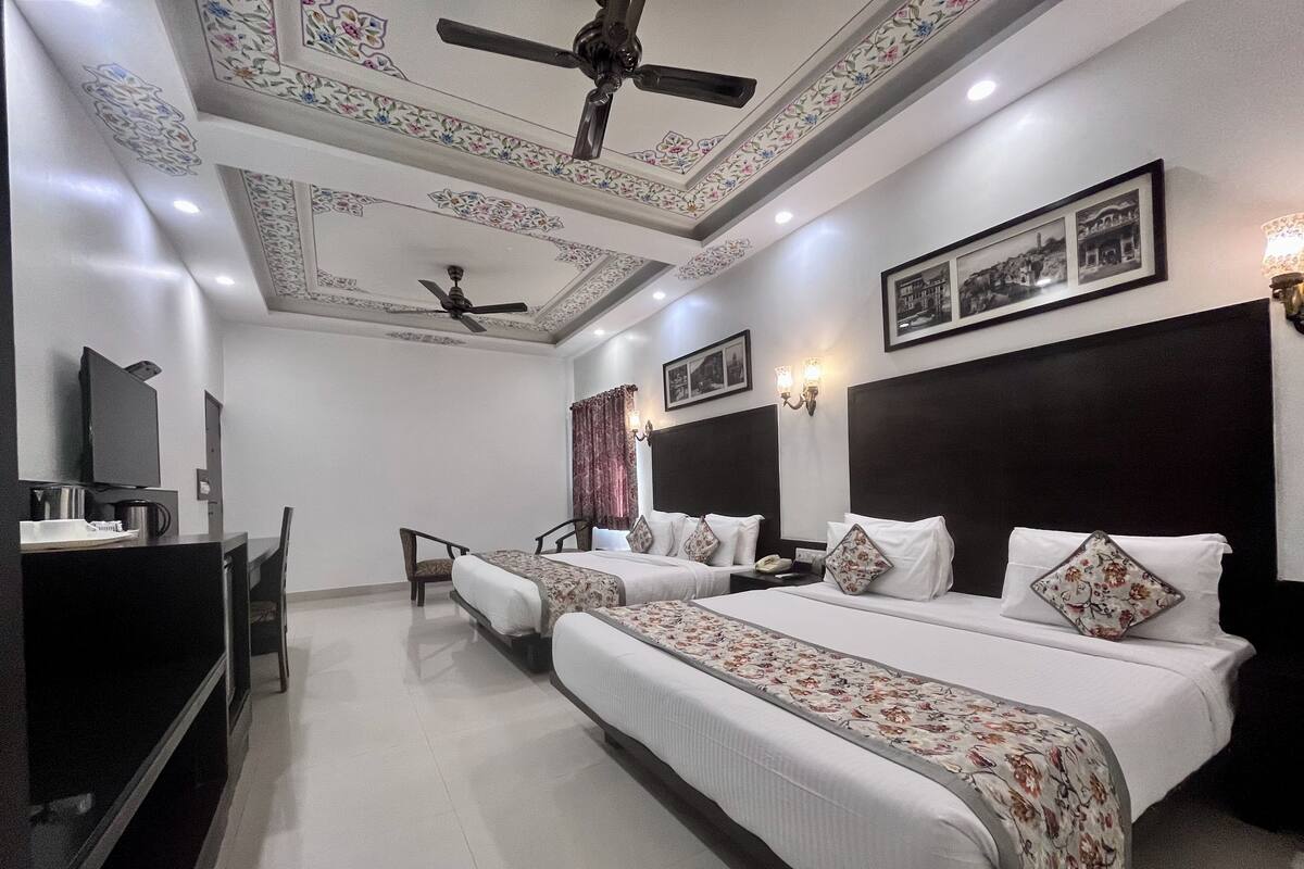A hotel room with two beds, a desk, a ceiling fan, and a television.