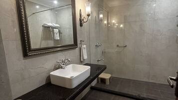 Un baño moderno con un espejo grande, un lavabo blanco y una ducha con mampara de cristal.