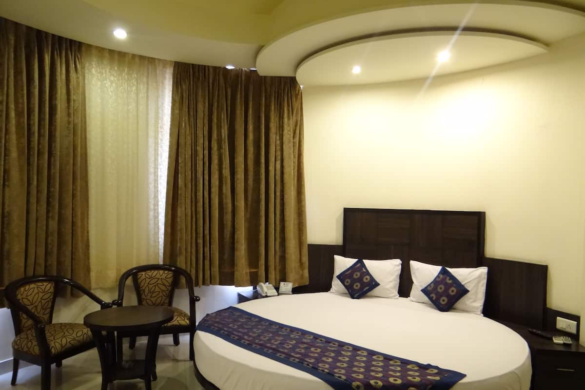A hotel room with a large bed, two chairs, a small table, and a nightstand with a phone.