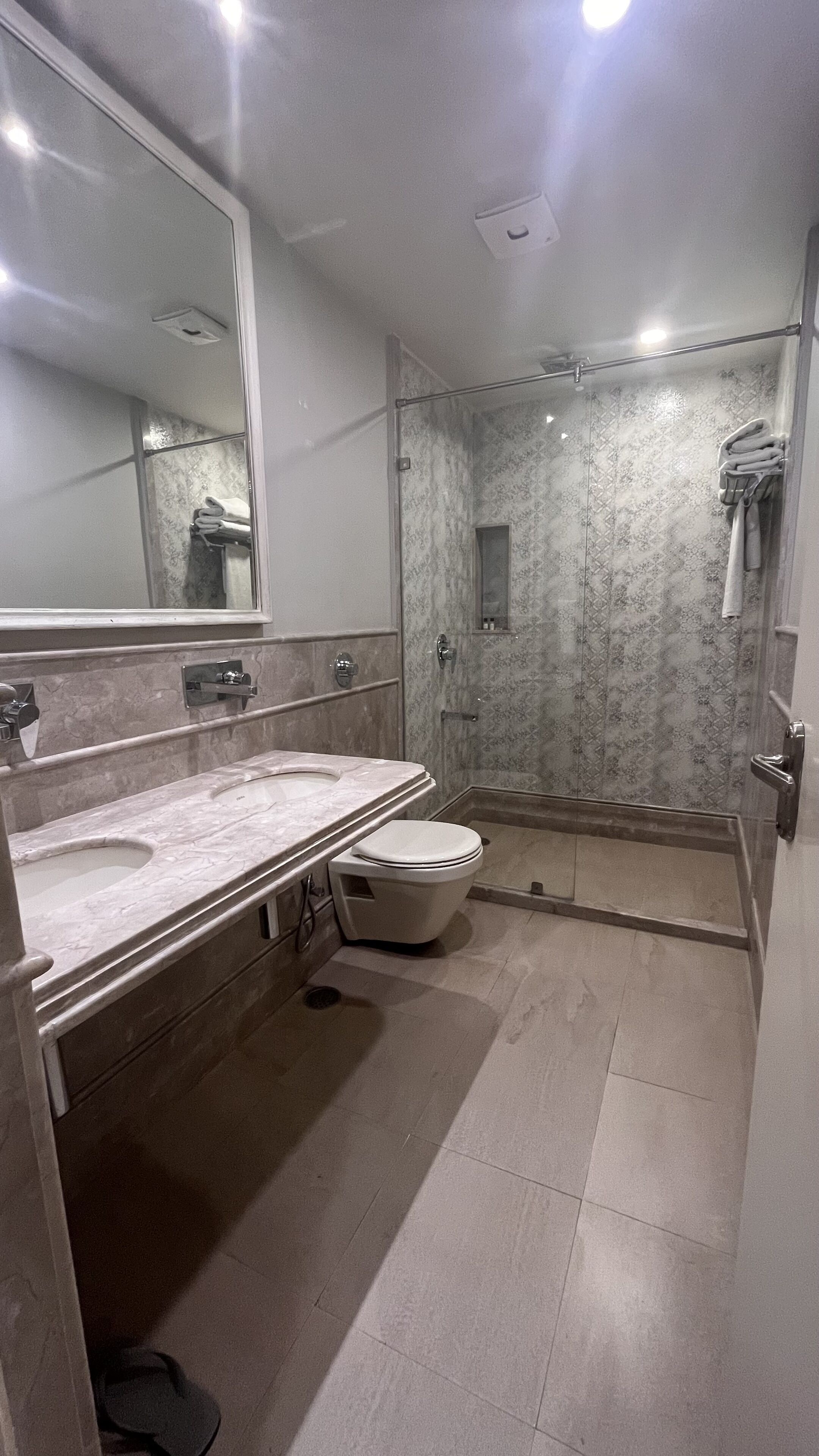 Un baño moderno con tocador de mármol, inodoro, ducha con mampara de vidrio y un espejo grande.