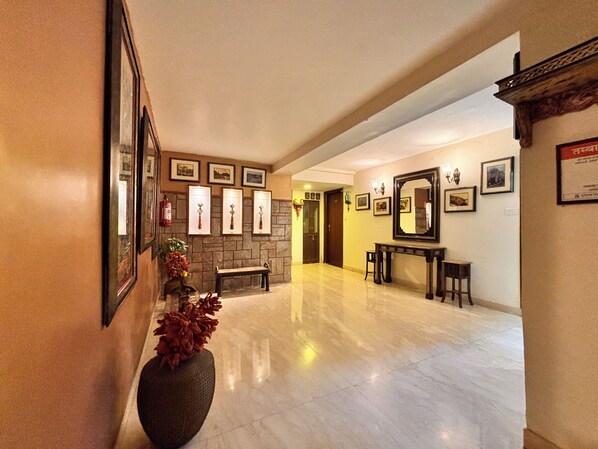 Um hall amplo com piso de mármore, lareira, quadros nas paredes e um espelho grande.