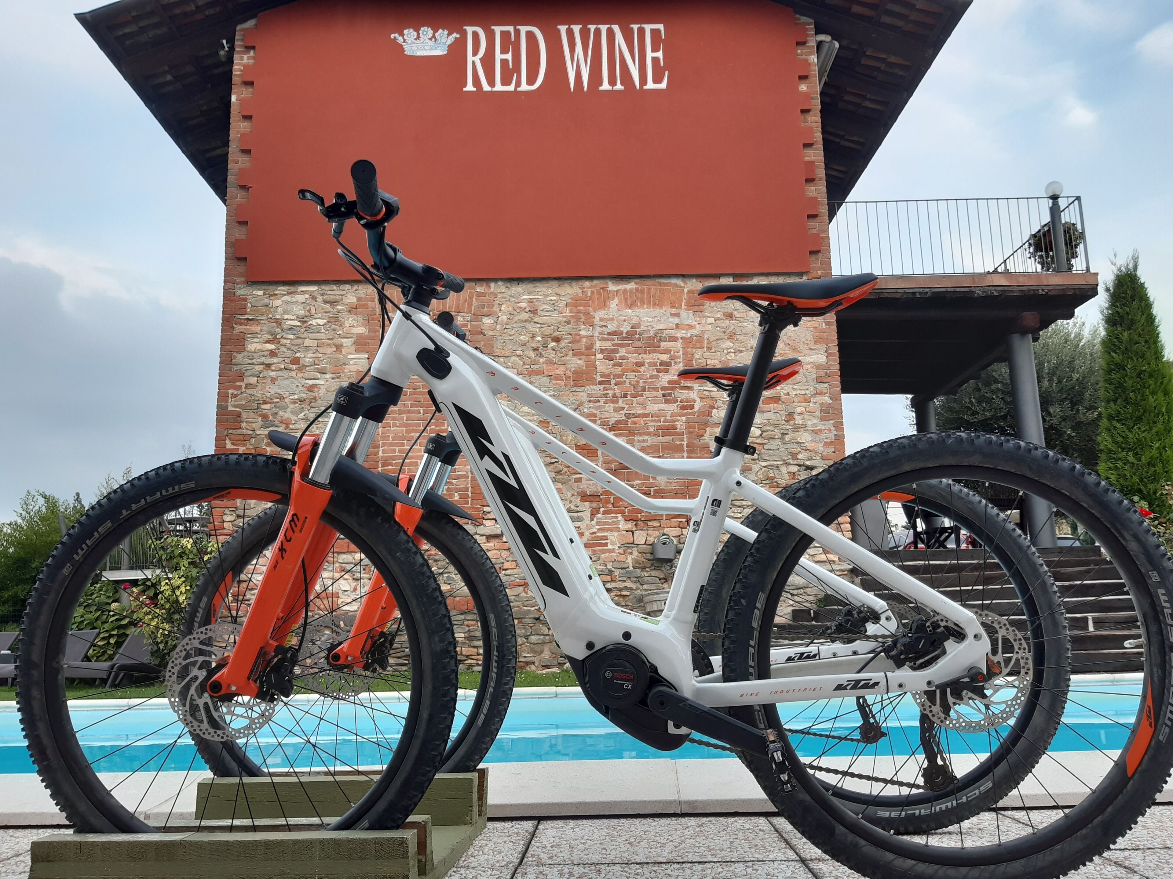 A mountain bike parked near a pool with a building labeled "RED WINE" in the background.