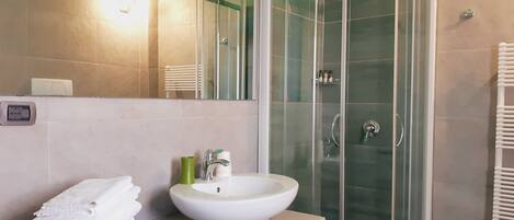 Un baño con ducha de vidrio, un lavabo blanco y una pila de toallas blancas sobre una mesa de vidrio.