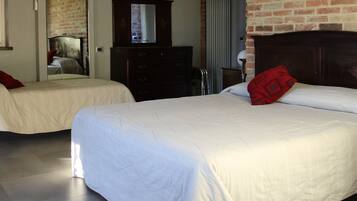 Dos camas individuales con ropa blanca y almohadas rojas, un aparador de madera y una pared de ladrillo.