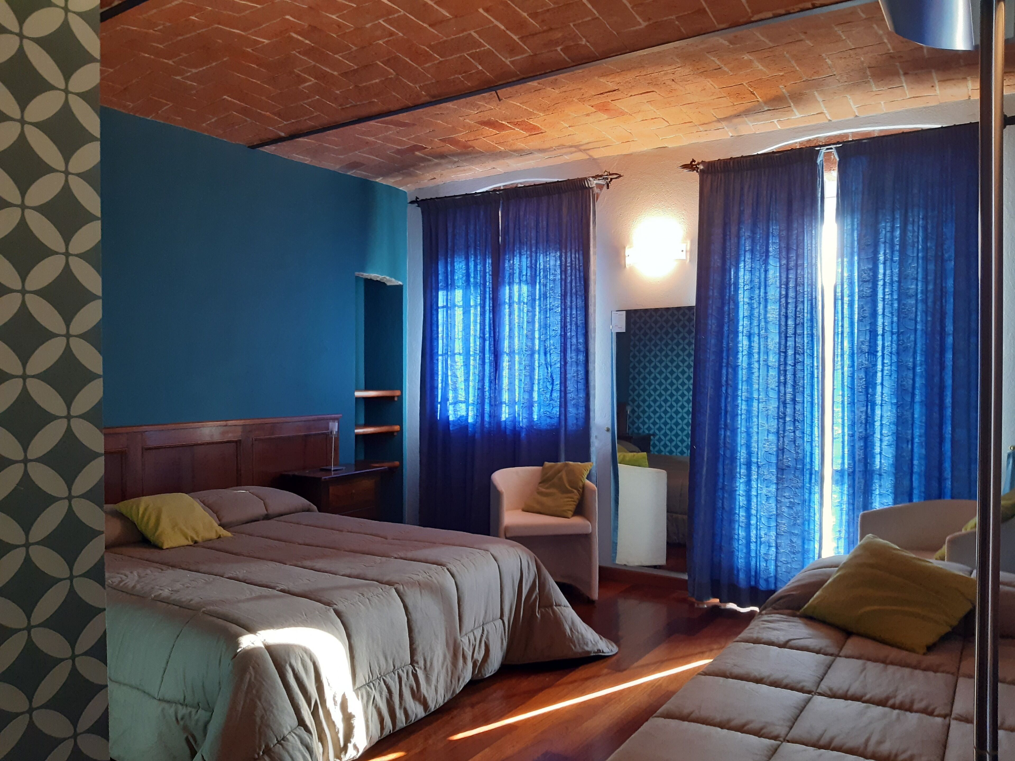 Une chambre avec deux lits, une chaise, une petite table et un mur bleu orné d’un motif géométrique.