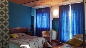 Une chambre avec deux lits, une chaise, une petite table et un mur bleu orné d’un motif géométrique.