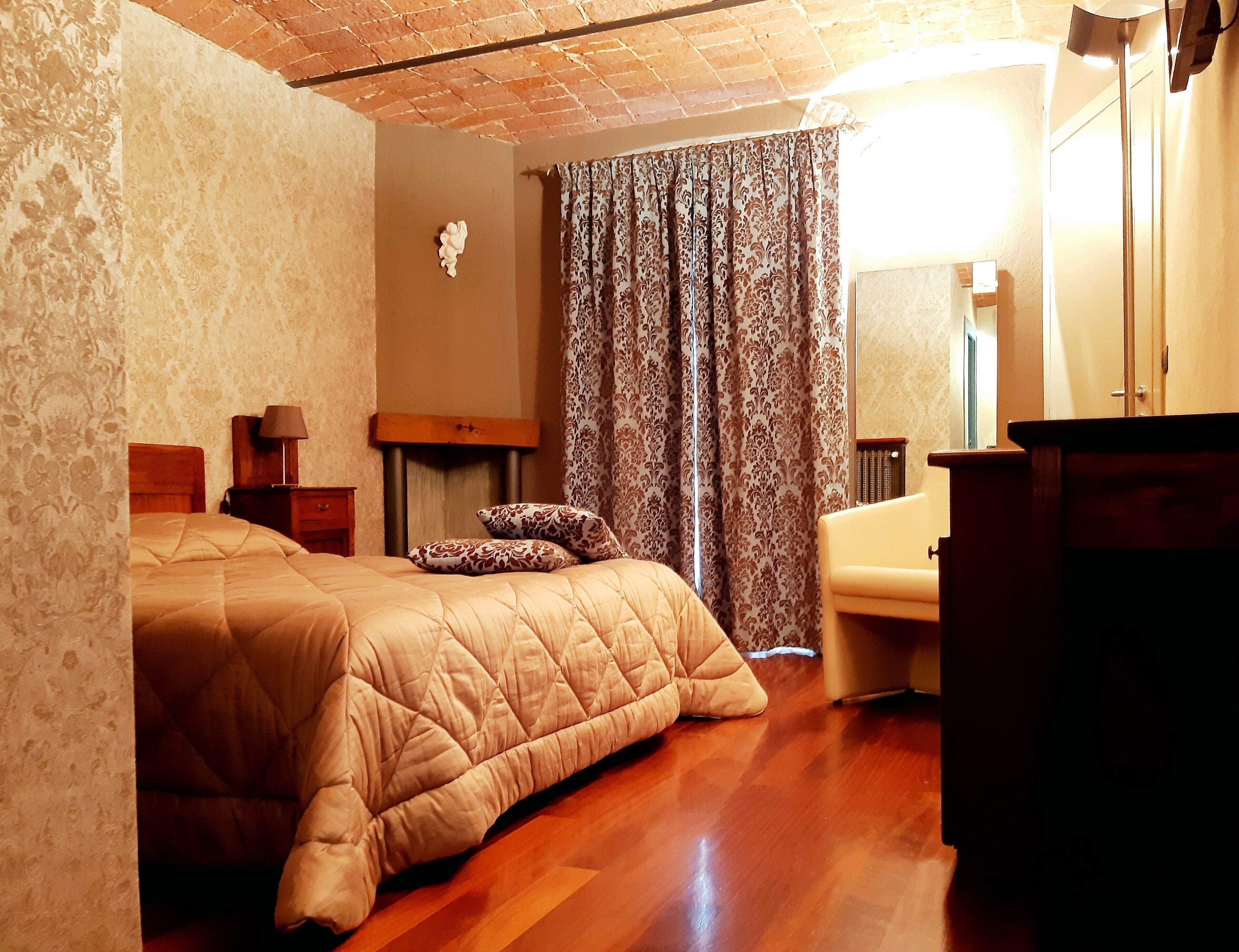 Une chambre à coucher avec un lit en bois, une table de chevet avec une lampe, un miroir et une fenêtre avec des rideaux.