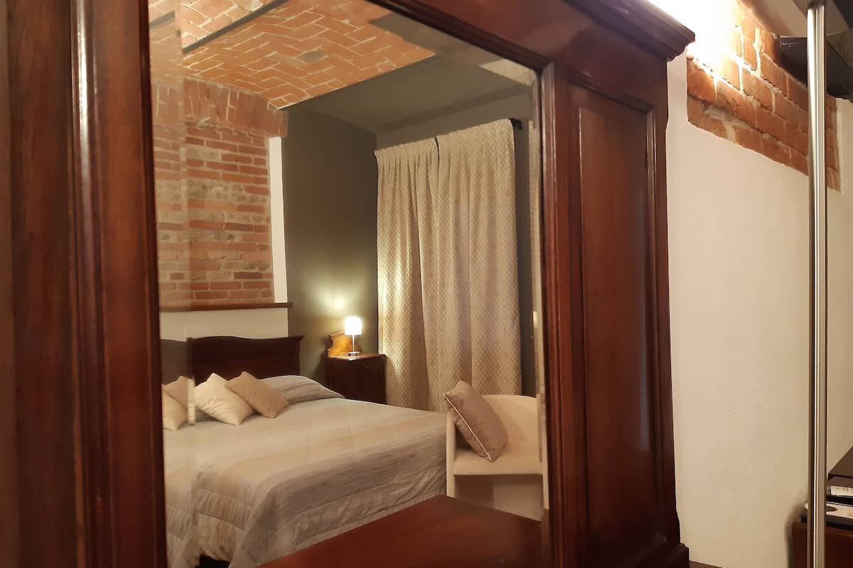 A bedroom with a wooden headboard, a bed with white bedding, a nightstand with a lamp, and a brick wall.